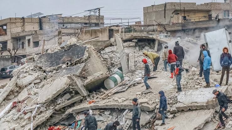 Group of people standing amongst rubble of destroyed buildings